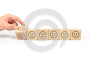 A hand chooses a smiley face on a cube made of wooden blocks, the best business service rating estimating the quality of customer