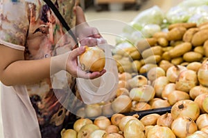 Hand choosing fresh onion from a basket in supermarket. Healthy lifestyle. A young woman chooses and buys onions in a fresh market