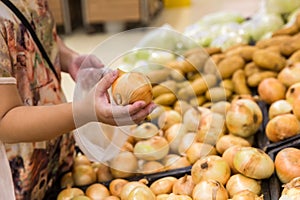 Hand choosing fresh onion from a basket in supermarket. Healthy lifestyle. A young woman chooses and buys onions in a fresh market
