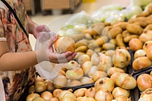 Hand choosing fresh onion from a basket in supermarket. Healthy lifestyle. A young woman chooses and buys onions in a fresh market