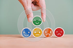 Hand choosing green happy smile face emoticon on circle wood, feedback rating and positive customer review, satisfaction survey
