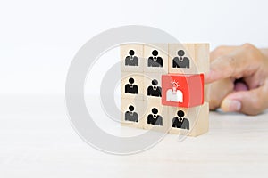 Hand choosing people head light bulb icon on cube wooden toy block stack in pyramid.