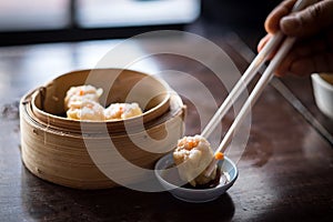 Hand with chopstick holding dimsum in to soy sauce