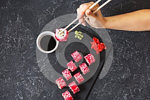 Hand with chopsticks on sushi set with soy sauce on black stone desk.