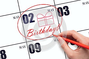 The hand circles the date on the calendar 2 May, draws a gift box and writes the text Birthday. Holiday.