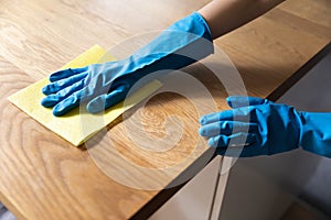 Hand of cleaner wearing blue protective rubber gloves, washing tabletop