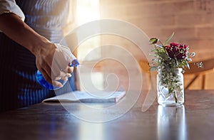 Hand, cleaning and coffee shop with a woman spraying a table in her restaurant for hygiene and sanitizing. Flowers, cafe