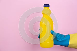 A hand with cleaning gloves holding a bottle of bleach on a pink background