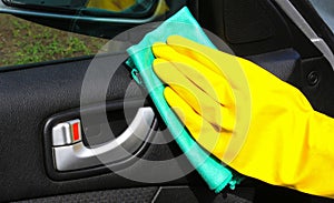 Hand cleaning interior car door panel with a green microfiber cloth in yellow gloves.