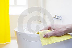 Hand cleaning a tub with a yellow wipe in a bright bathroom