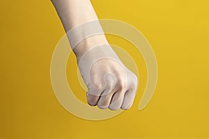 Hand with clenched fists against yellow background