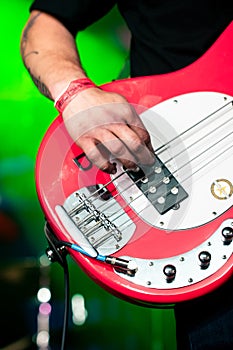 Hand Close Up Playing the Red Bass Guitar with Green stage Lights