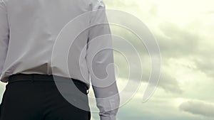 Hand close-up. Serious man in white shirt with briefcase in his hand goes to work against background of gloomy dark sky