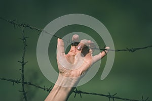 Hand clutch at barbed wire fence on green background - vintage r