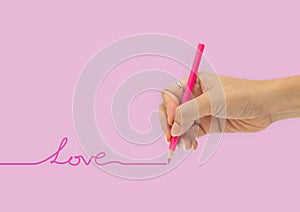 Hand with color pencil is writing love line isolated on pink ba