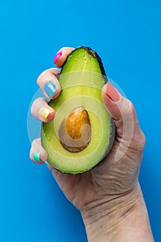 A hand with colourful nail polish holding a fresh cut avocado.