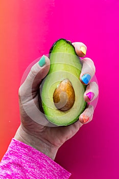 A hand with colourful nail polish holding a freshly cut avocado.