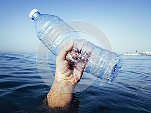 Hand coming out of the ocean with a plastic bottle