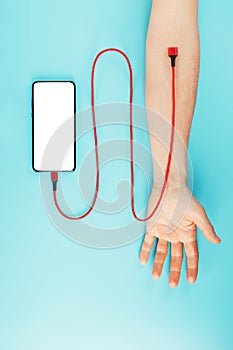 The hand is connected by a red power cord to a smartphone with free space on a blue background.