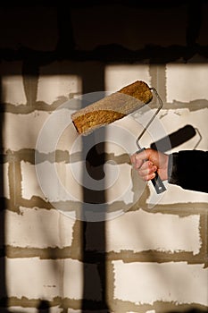 Hand with a construction roller with a fur nozzle on the background of a wall of aerated concrete blocks.