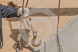 The hand of construction worker male take a heavy iron hook lifting mechanism with a steel cable rope to a concrete, cement