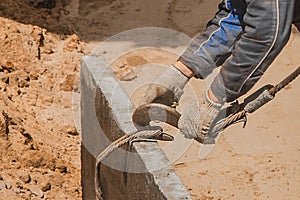 The hand of construction worker male take a heavy iron hook lifting mechanism with a steel cable rope to a concrete, cement