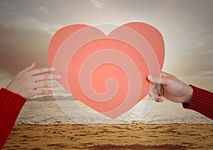Hand of couple holding red heart on beach