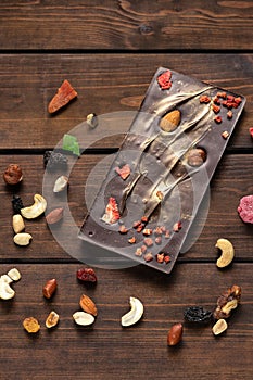 Hand crafted dark chocolate with almond, orange and dried fruits on a wooden background