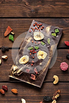 Hand crafted dark chocolate with hazelnut, banana and dried fruits on a wooden background