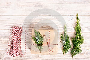 Hand crafted gift box on rustic white wooden background with Christmas decoration fir tree top view. Toned