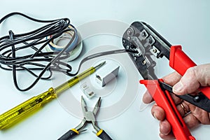 Hand of a craftsman with a crimping tool connecting an RJ45 connector with a black cable on a white background with a screwdriver