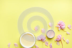 Hand cream, lip balm on a yellow background, flower petals. Space for a text.