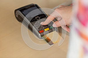 Hand with credit card swipe through terminal for payment in cafe.