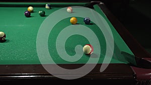 Hand with cue aiming on billiard ball at table, hit balls in the hole.