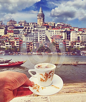 Hand with a cup of coffee with Istanbul riverside on a background. Travel concept