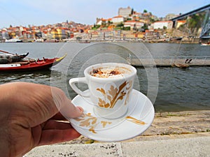 Hand with a cup of coffee and view of Douro riverside from the Dom Luiz bridge , Porto , Portugal.