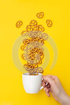 A hand and cup with effuse pretzels on yellow background, flat lay.