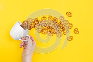 A hand and cup with effuse pretzels on yellow background, flat lay.