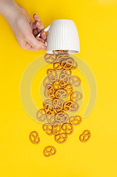 A hand and cup with effuse pretzels on yellow background, flat lay.