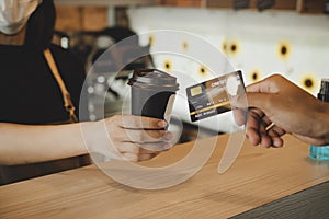 Hand customer paying with credit card for buying hot coffee cup on counter in modern cafe coffee shop