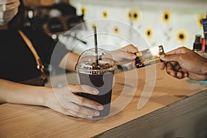 Hand customer paying with credit card for buying ice black coffee on counter in modern cafe coffee shop