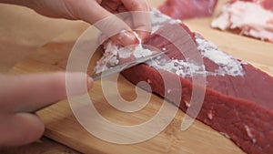 A hand cuts off fat and veins from red beef meat. Preparation of ingredients