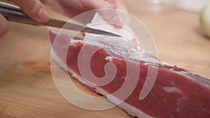 A hand cuts off fat and veins from red beef meat. Preparation of ingredients