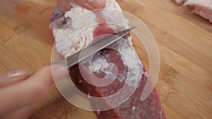 A hand cuts off fat and veins from red beef meat. Preparation of ingredients