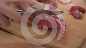 A hand cuts off fat and veins from red beef meat. Preparation of ingredients