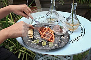Hand cutting waffle with kiwi and ice cream on black plate. Waffle with honey. Dessert sweetness.