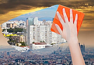 Hand deletes smog in city by orange cloth