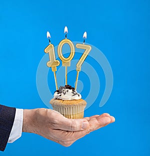 Hand delivering birthday cupcake - Candle number 107 on blue background