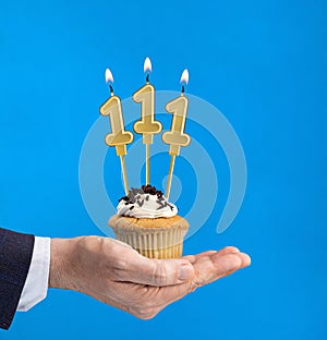 Hand delivering birthday cupcake - Candle number 111 on blue background