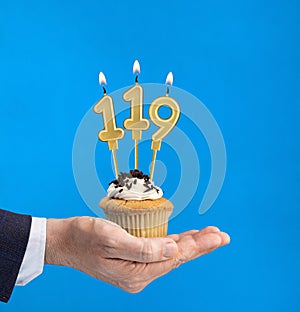Hand delivering birthday cupcake - Candle number 119 on blue background